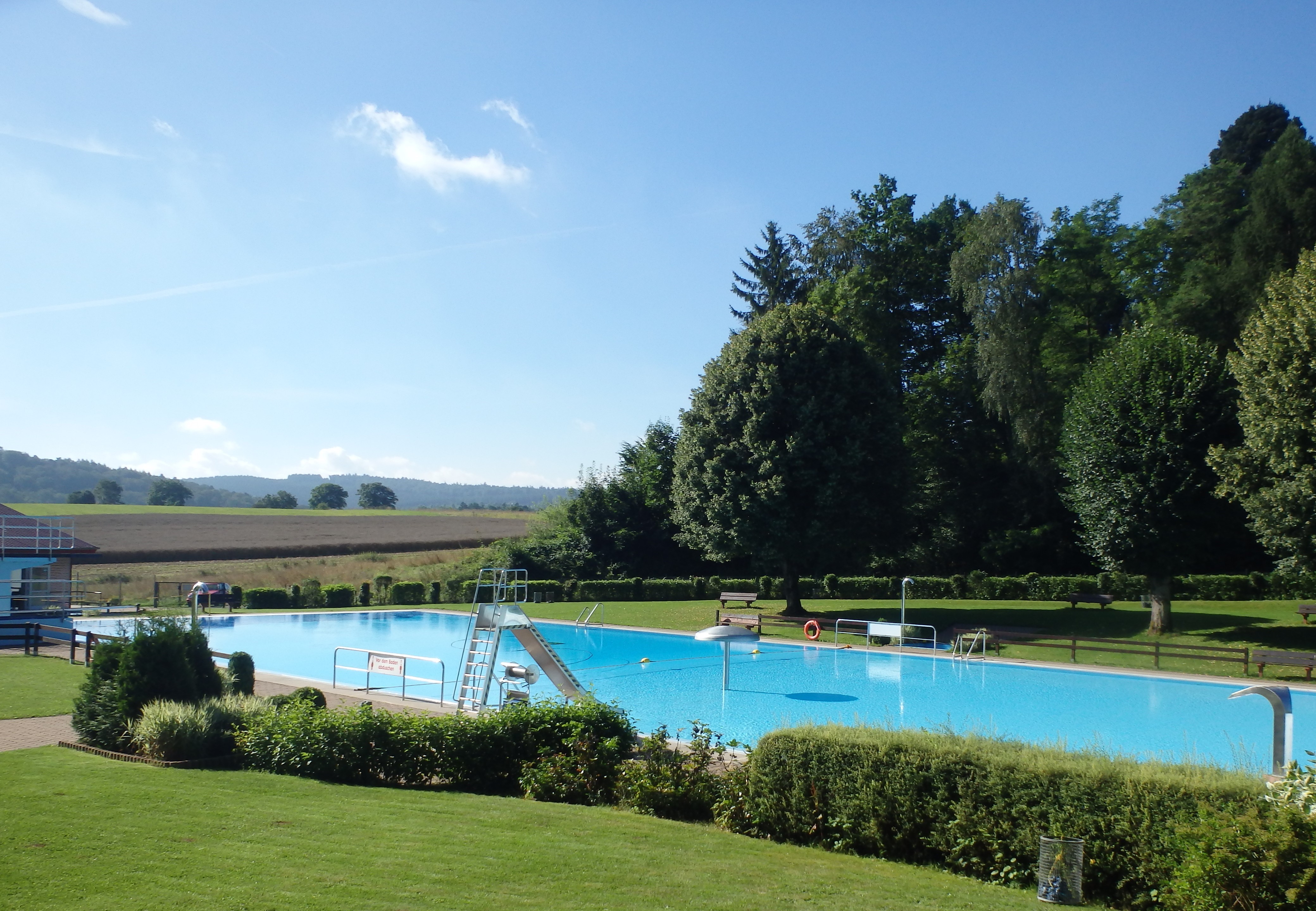 Schwimmbecken; im Hintergrund Wald und Feld